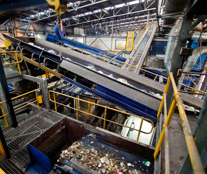 An industrial recycling facility with conveyor belts and machinery sorting waste materials, including food scraps and plastic debris.