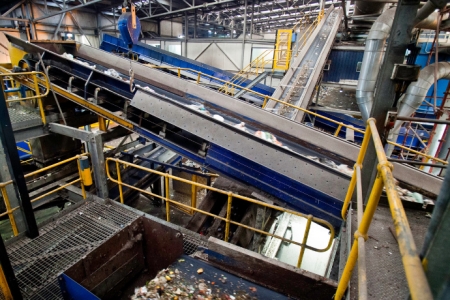 An industrial recycling facility with conveyor belts and machinery sorting waste materials, including food scraps and plastic debris.