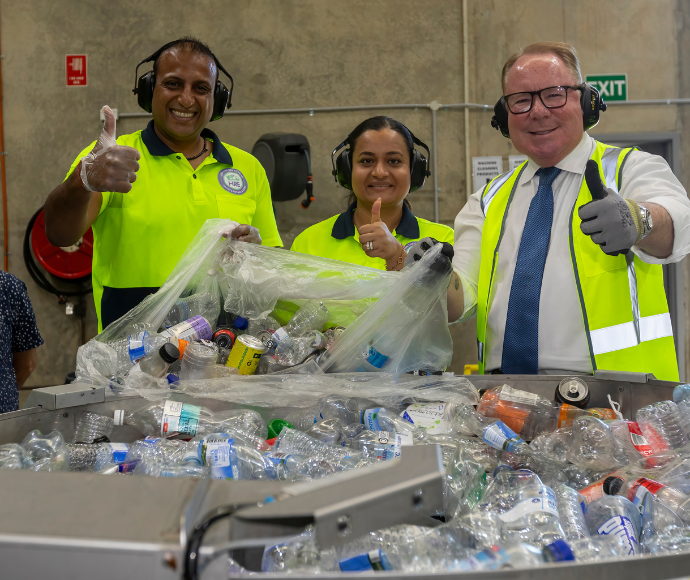 Three people in high vis clothes in front of a pile of recycled plastic bottles.