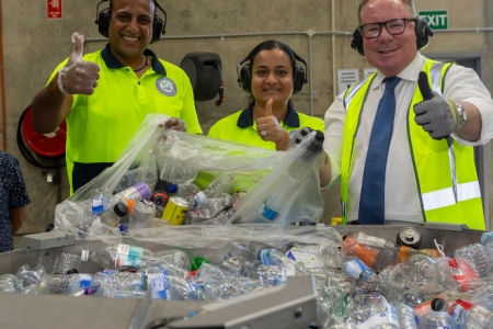 Three people in high vis clothes in front of a pile of recycled plastic bottles.