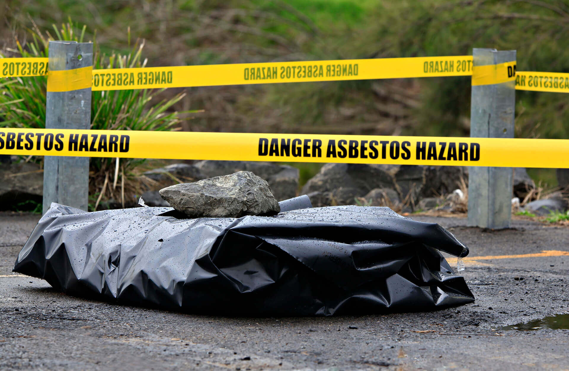 Asbestos waste wrapped in black plastic with Dangerous asbestos hazard tape