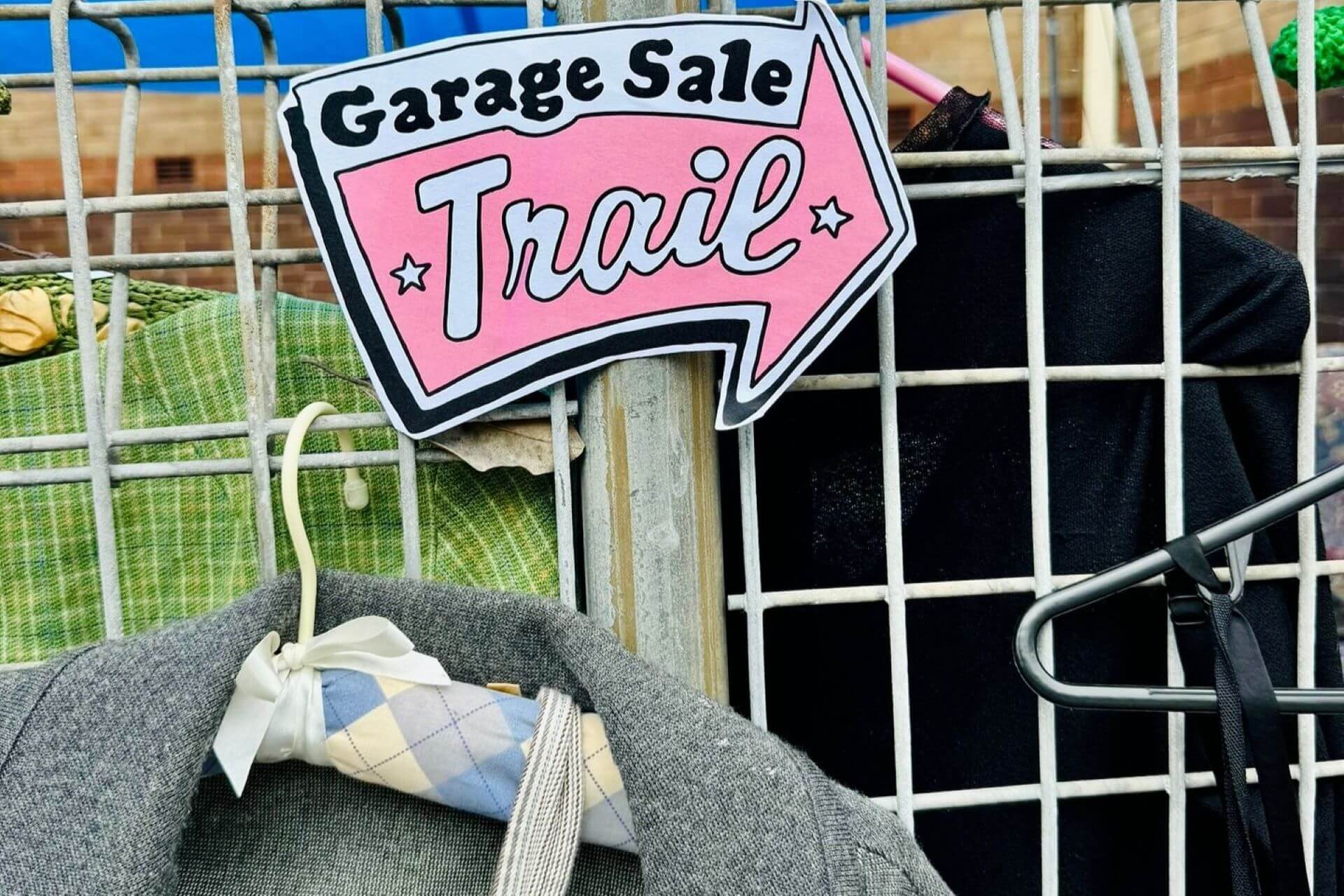 Secondhand jackets hanging on a metal frame underneath a sign which reads Garage Sale Trail