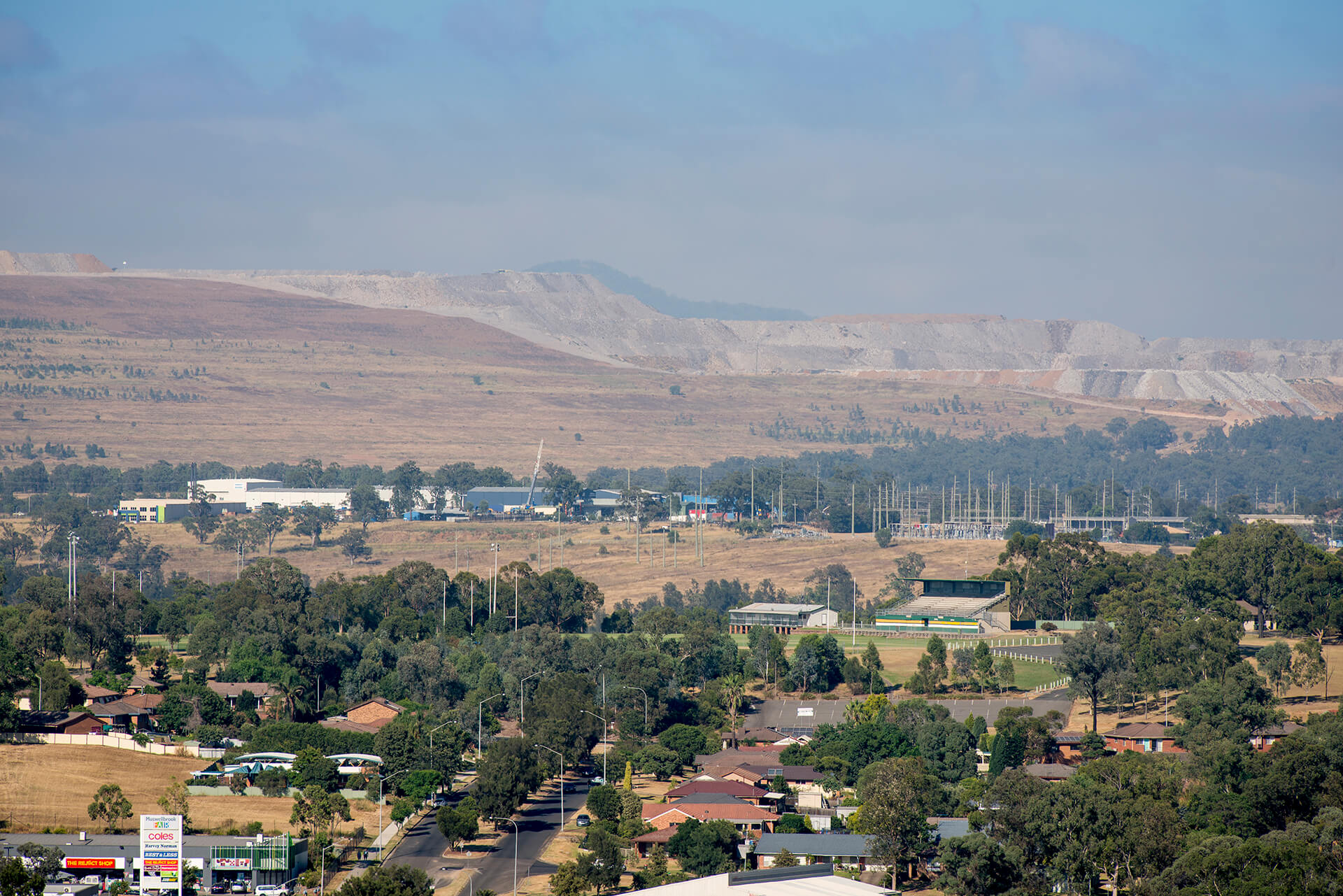 Residential area in the foreground, with open cut coal mine in the background and hazy air, Hunter Valley