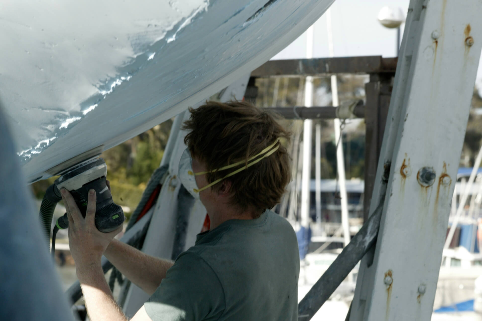 Person wearing dust-mask sanding marine anti-foul paint from a boat hull