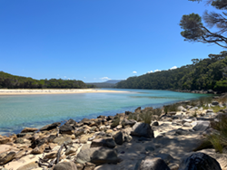 The Nadgee River bank with rocks, beach in the distance and blue skies